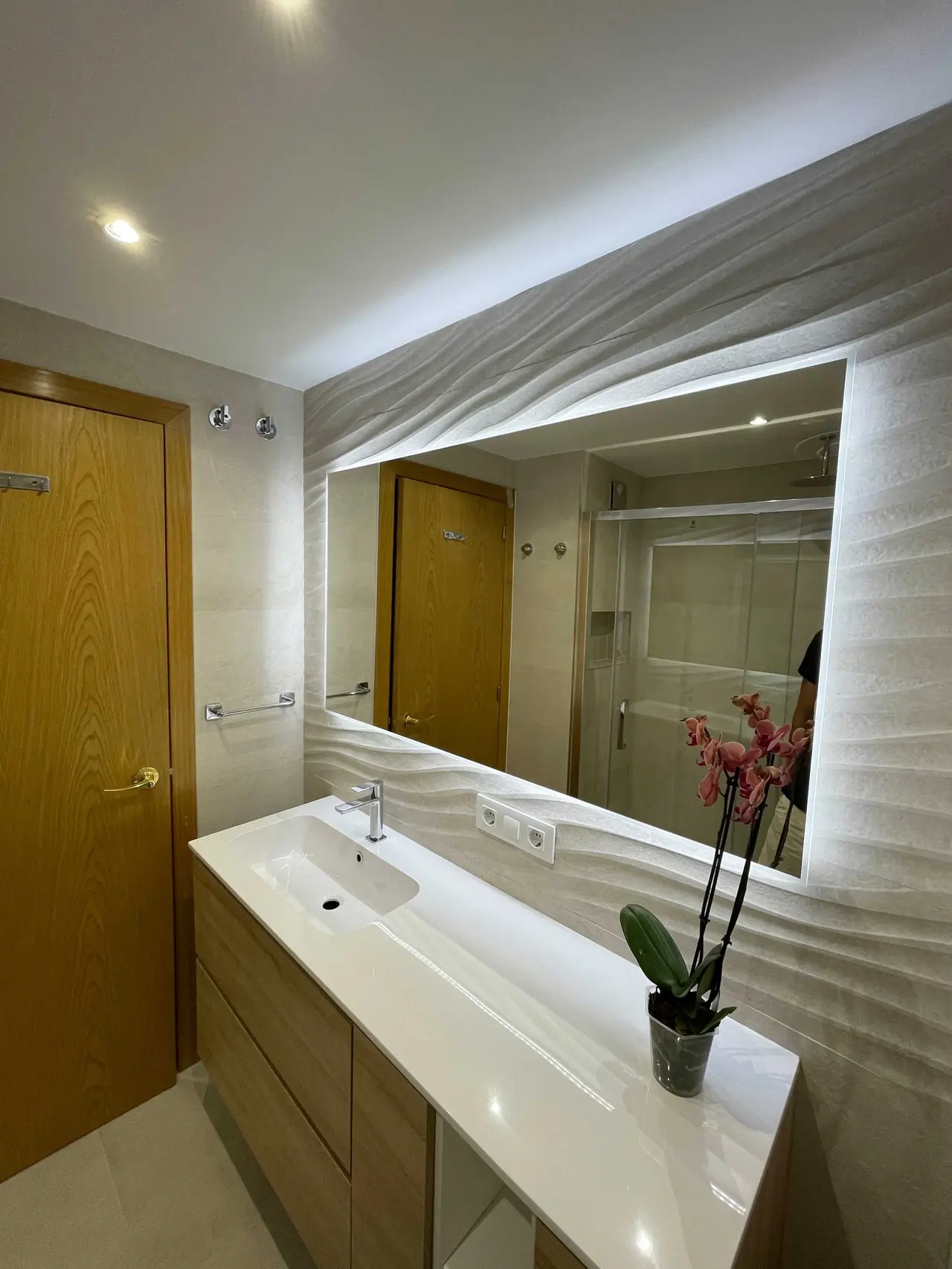 Baño con espejo ondulado y mueble de madera